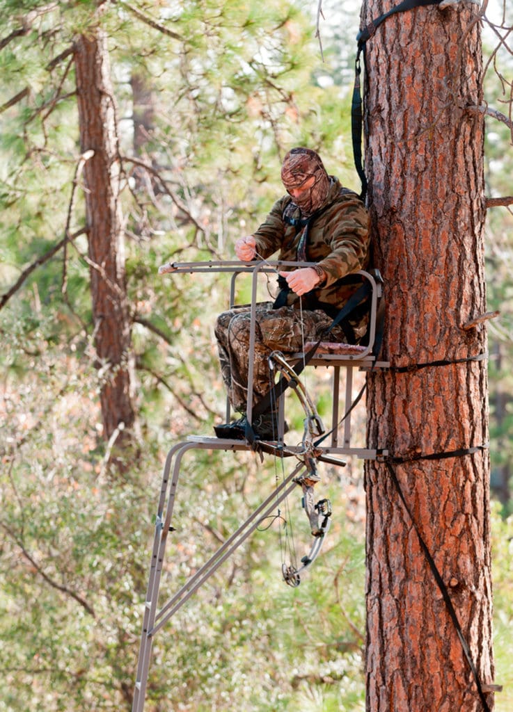 Bågjägare med säkerhetssele på kroppen och en lina runt trädstammen, som ska hindra fall ner på marken från jaktstegen.